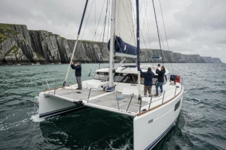Catamaran blanc naviguant le long des côtes granitiques de Bretagne avec vue sur les falaises et la mer émeraude