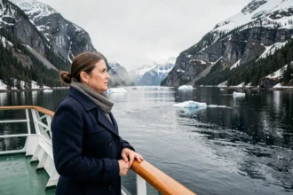 Femme en manteau de laine sur le pont d'un bateau de croisière contemplant un fjord norvégien enneigé